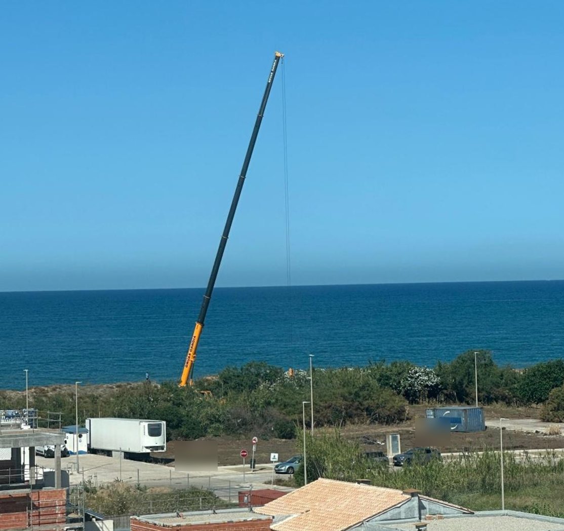 Grúa elevada visible sobre vegetación próxima a la duna