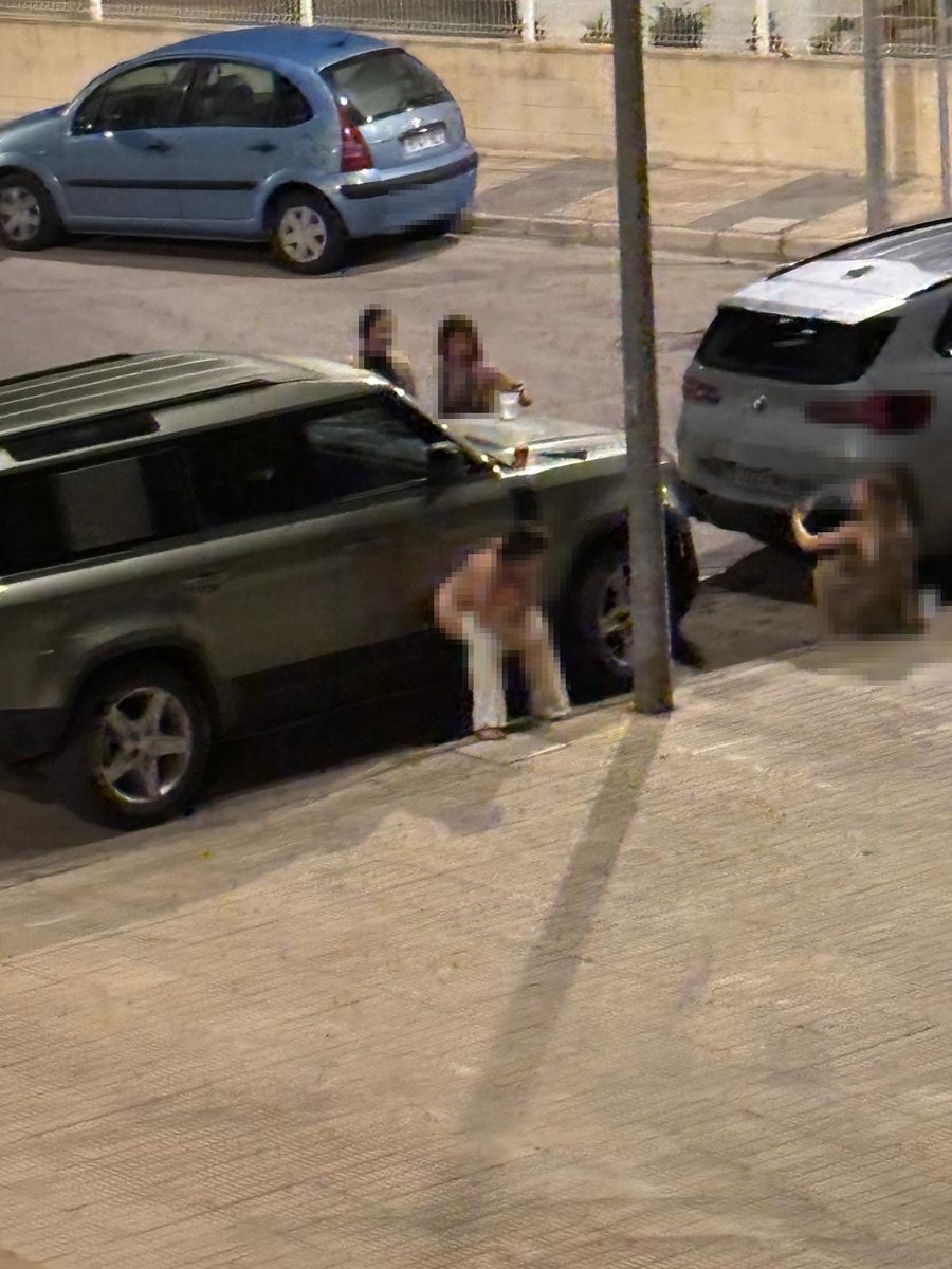 Personas reunidas de madrugada en la vía pública entre vehículos estacionados en Playa Terranova, con rostros y matrículas pixelados